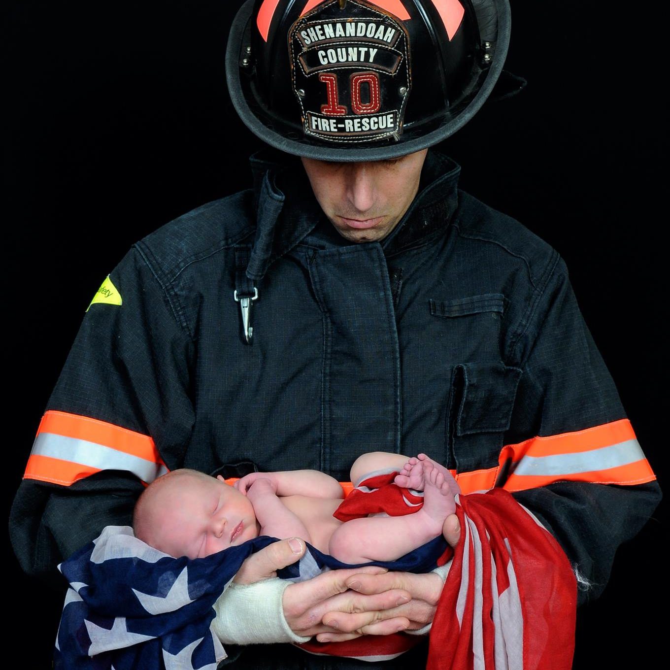 Photo of newborn wrapped in flag held by firefighter